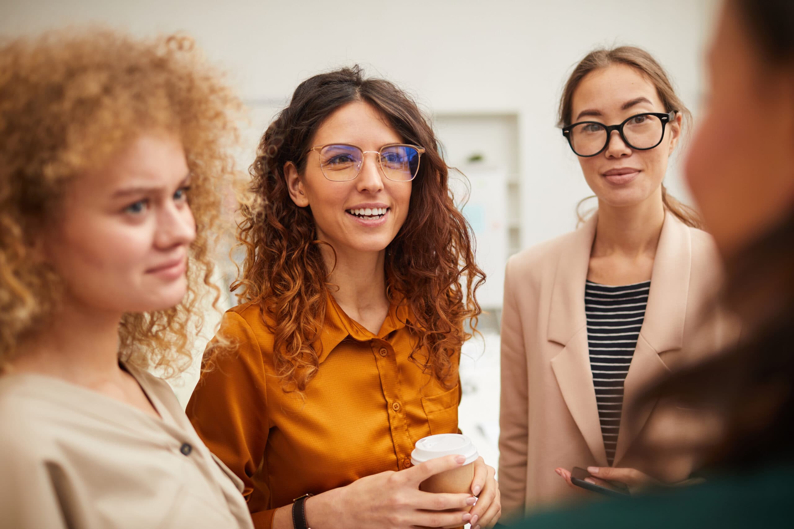 Group of four cheerful young women chatting during break, horizontal shot